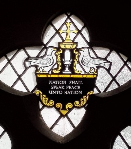 Stained glass window featuring a BBC microphone, doves of peace and the caption Nation Shall Speak Peace Unto Nation